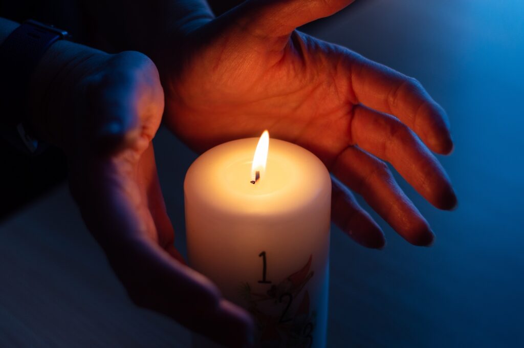 Burning candle with number 1 and hands warming near flame