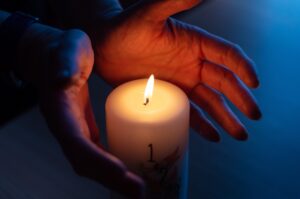 Burning candle with number 1 and hands warming near flame